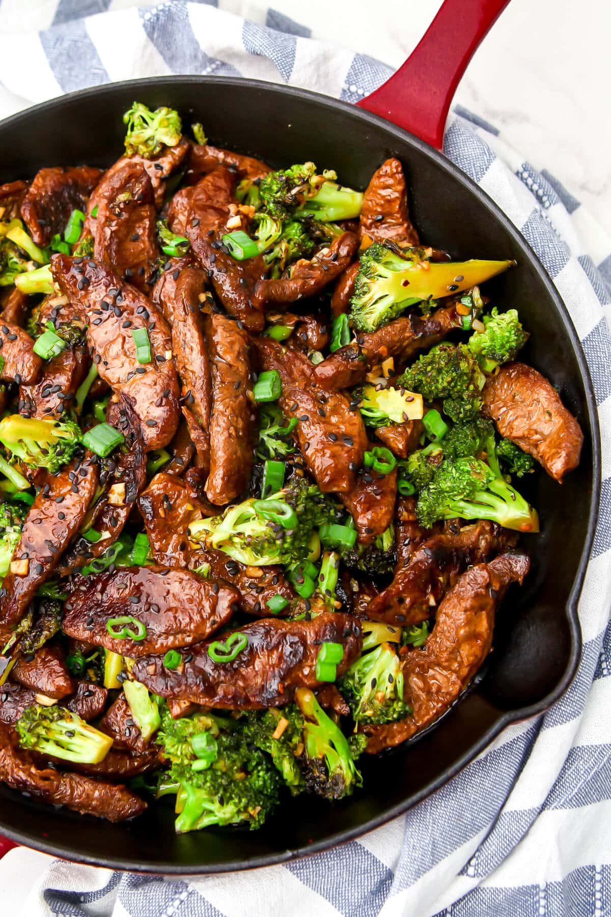 A skillet full of vegan beef and broccoli stir fry garnished with sesame seeds and green onions.