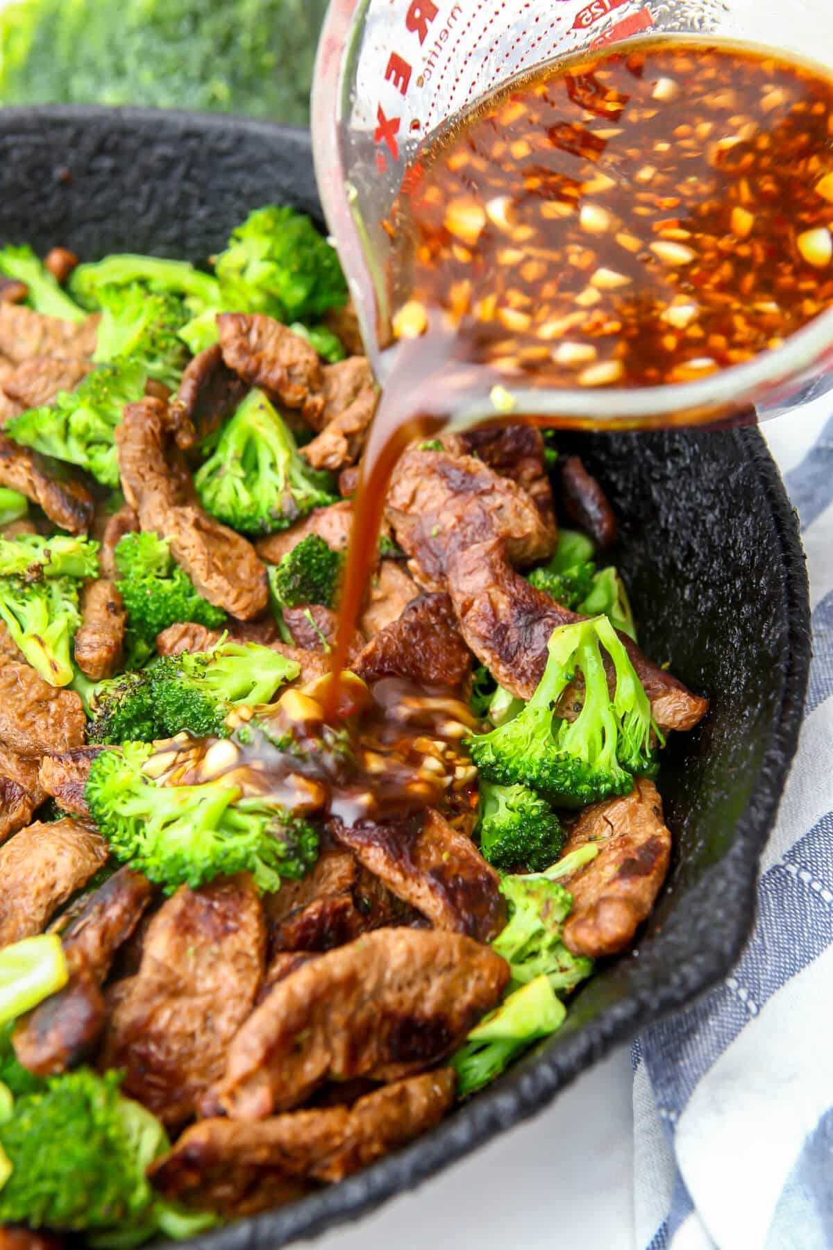 Stir fry sauce being poured over vegan beef strips cooked with broccoli.
