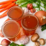 Homemade vegetable broth in 3 mason jars with vegetables around them.