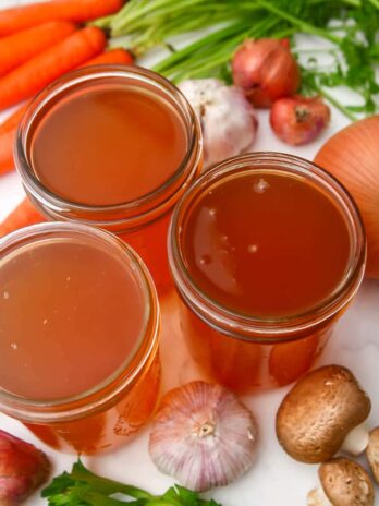 Homemade vegetable broth in 3 mason jars with vegetables around them.