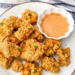 Tofu fried chicken nuggets on a white plate with a small bowl of dipping sauce at the side.