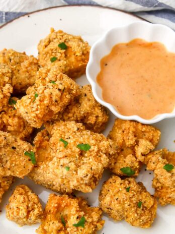 Tofu fried chicken nuggets on a white plate with a small bowl of dipping sauce at the side.