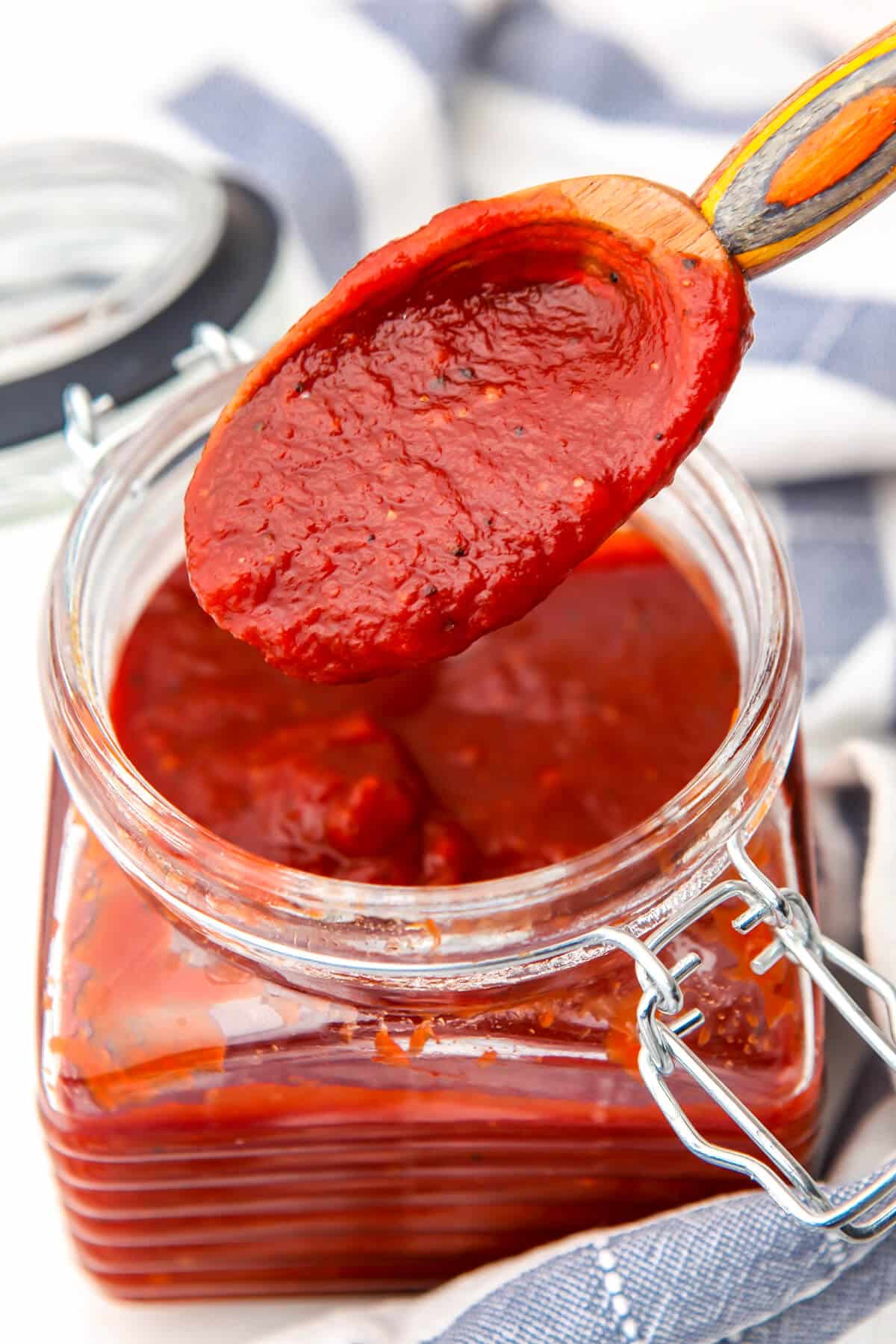 Vegan bbq sauce in a glass jar with a spoon scooping up some sauce.