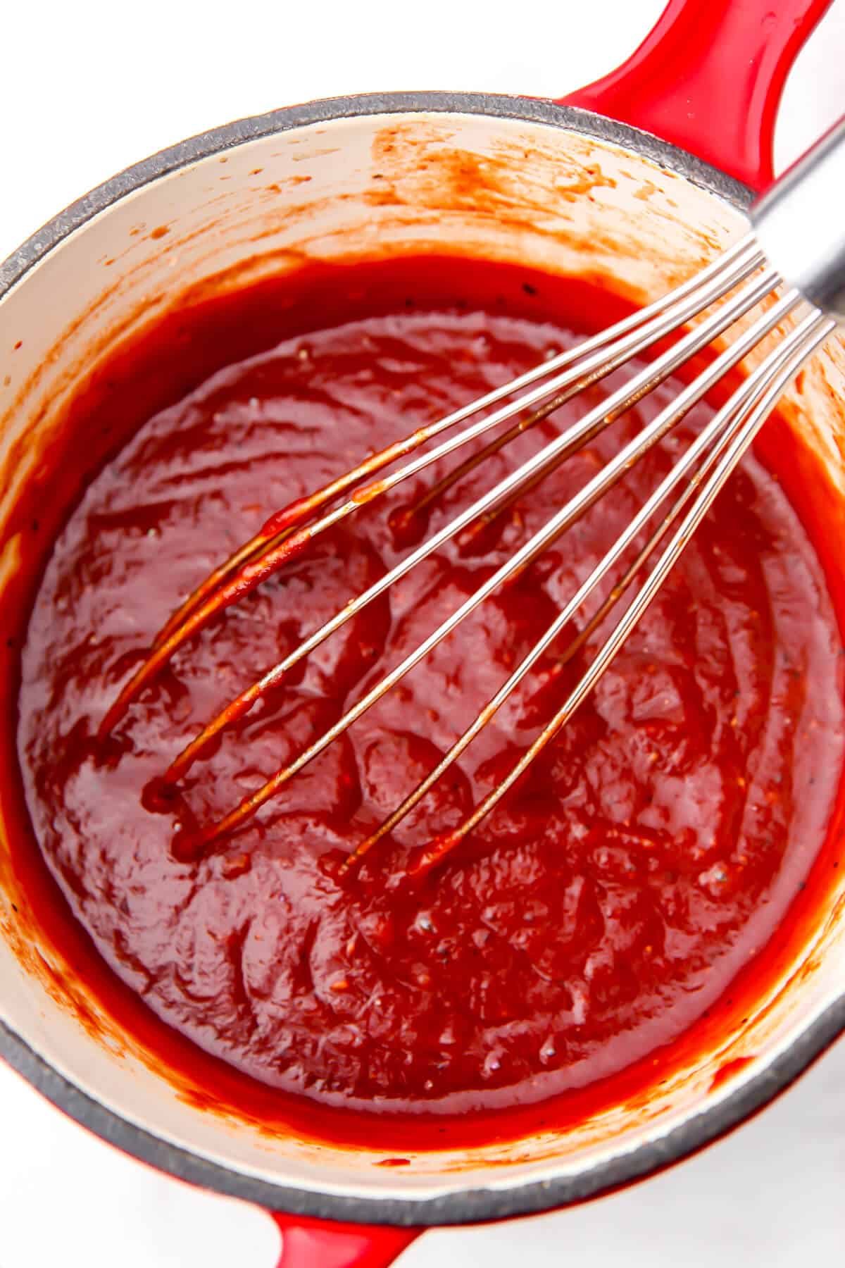 Vegan BBQ sauce in a saucepan being stirred with a whisk.