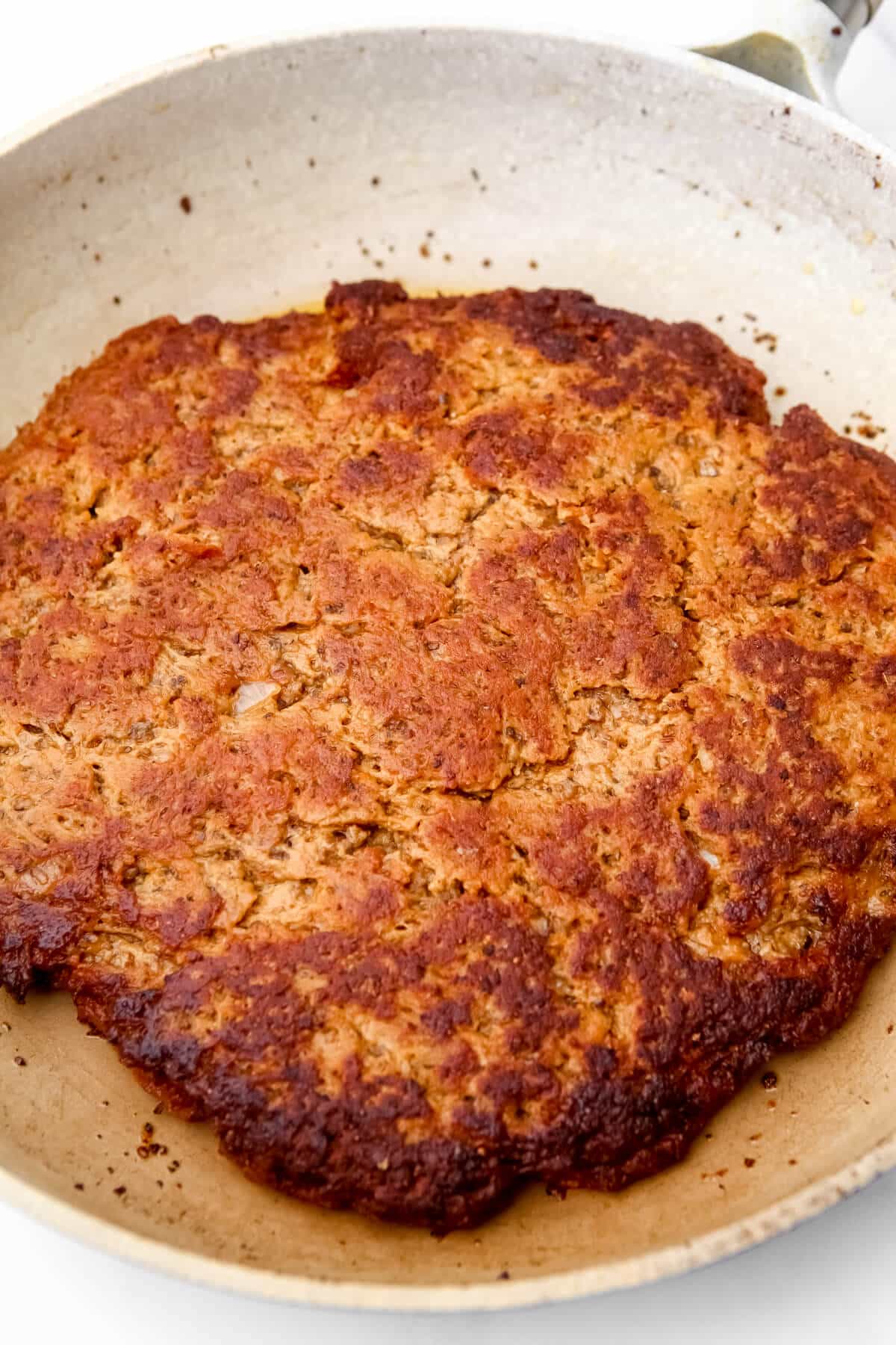 A large round of seitan frying in a skillet.