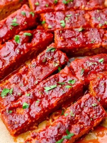 Vegan ribs smothered in BBQ sauce on a piece of parchment paper.