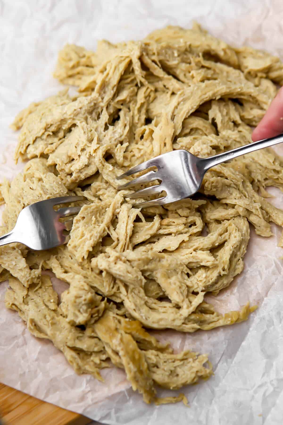 Vegan chicken seitan being shredded with two forks on a cutting board.