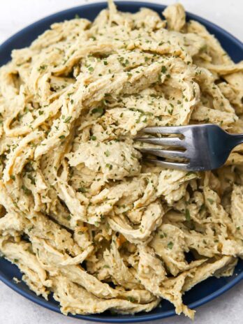 Vegan shredded chicken made from seitan on a blue plate with a fork in it.