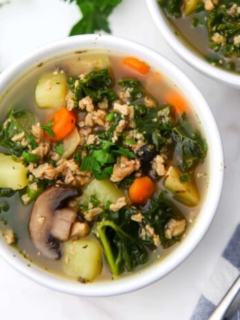 A bowl of vegan stew with mushrooms, kale, potatoes, and carrots.