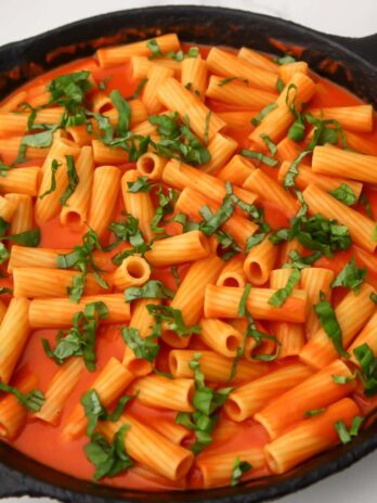 An iron skillet full of vegan vodka pasta topped with fresh basil.