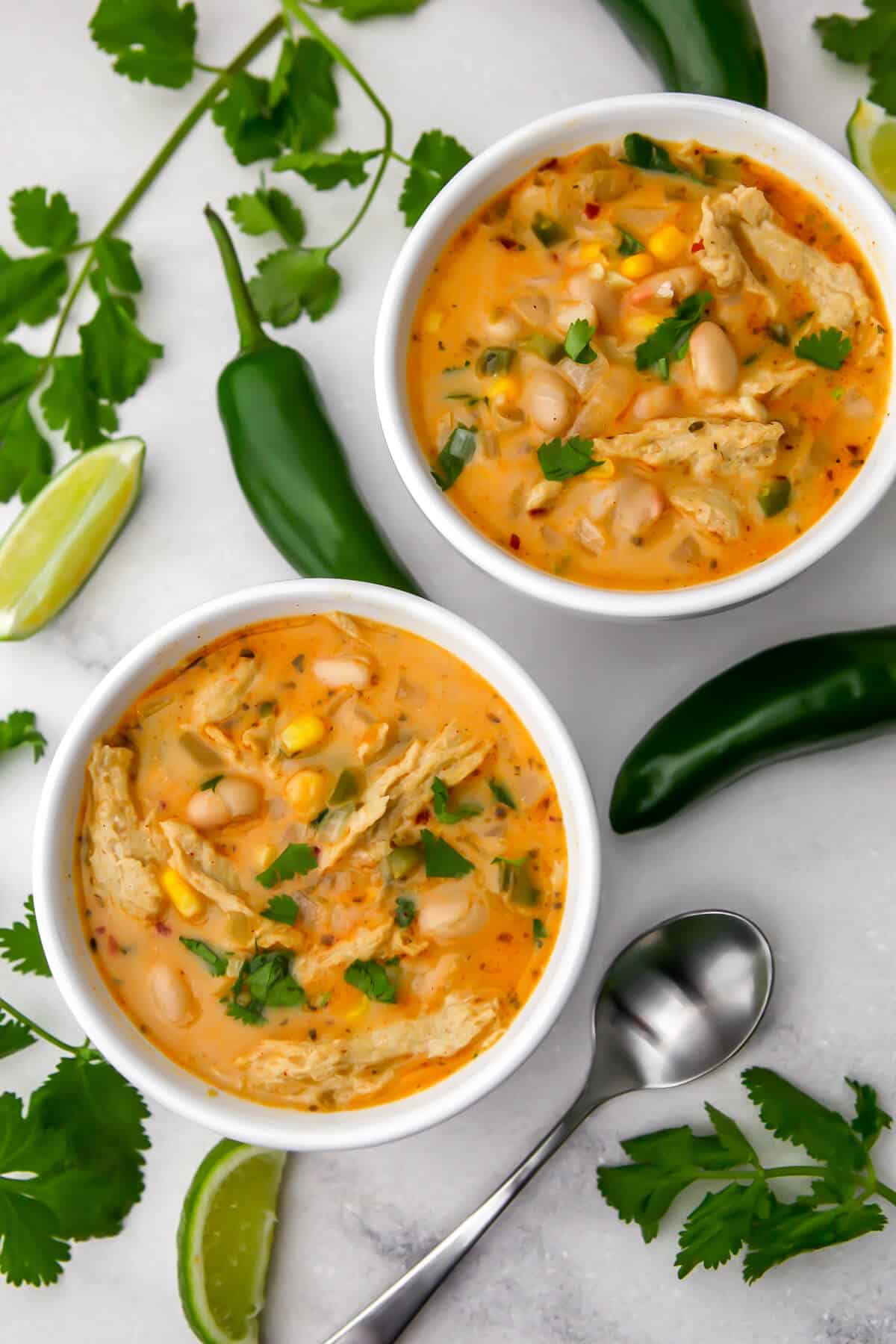 Two bowls of vegan white chili with vegan chicken with jalapeno, lime wedges, and cilantro.