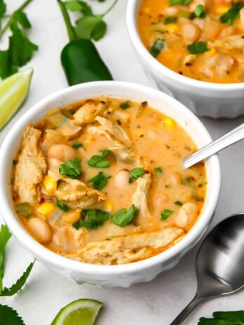 A top view of two bowls of vegan white chili with cilantro and jalapeno peppers on the side.