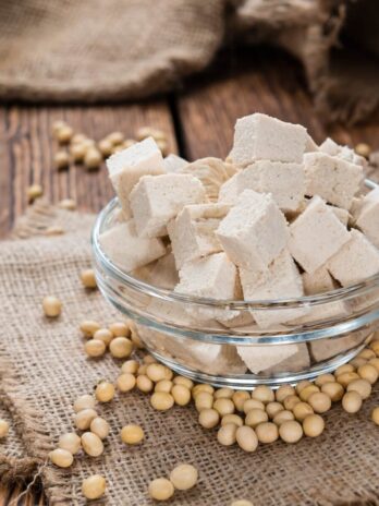 A bowl of tofu with soy beans around it on a burlap placemat.