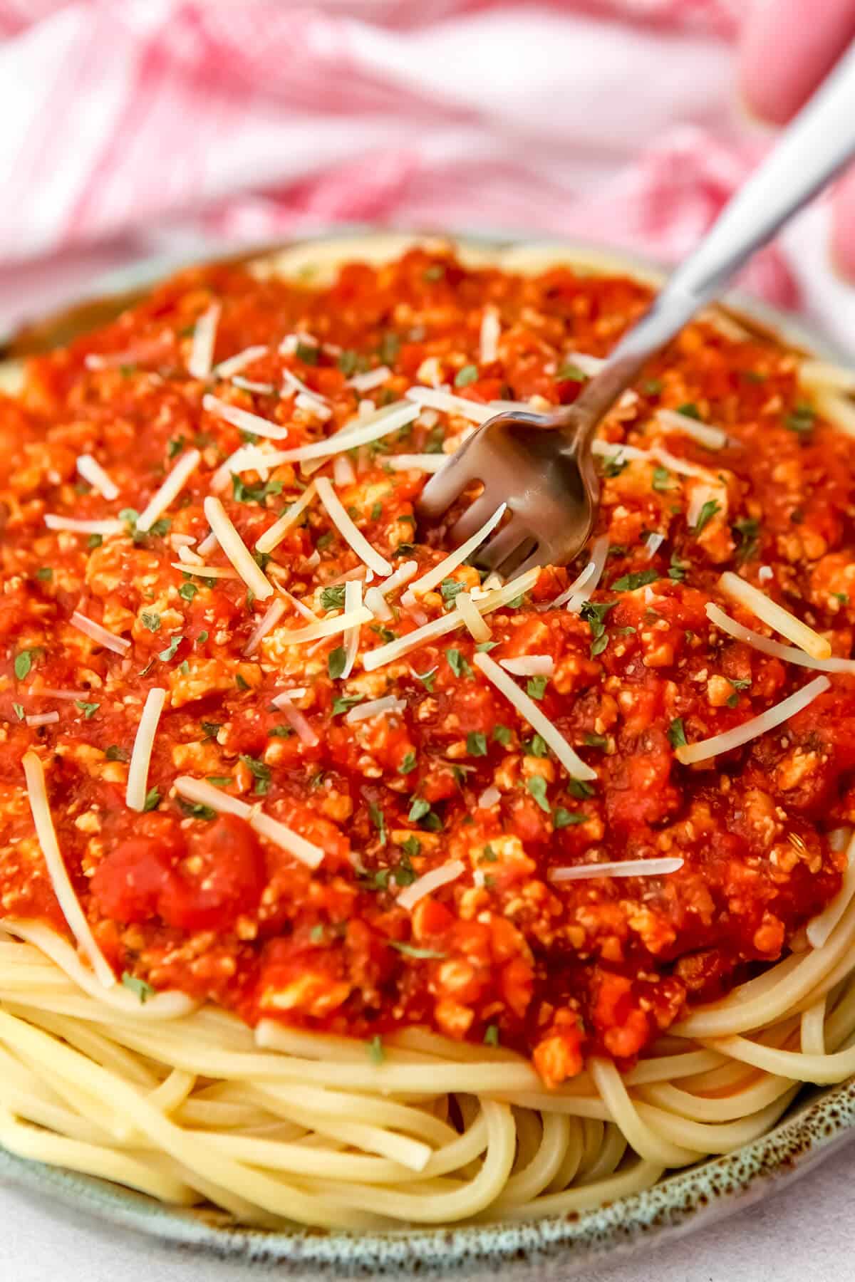 A plate of speghetti with tofu Bolognese over it with a fork sticking in it.