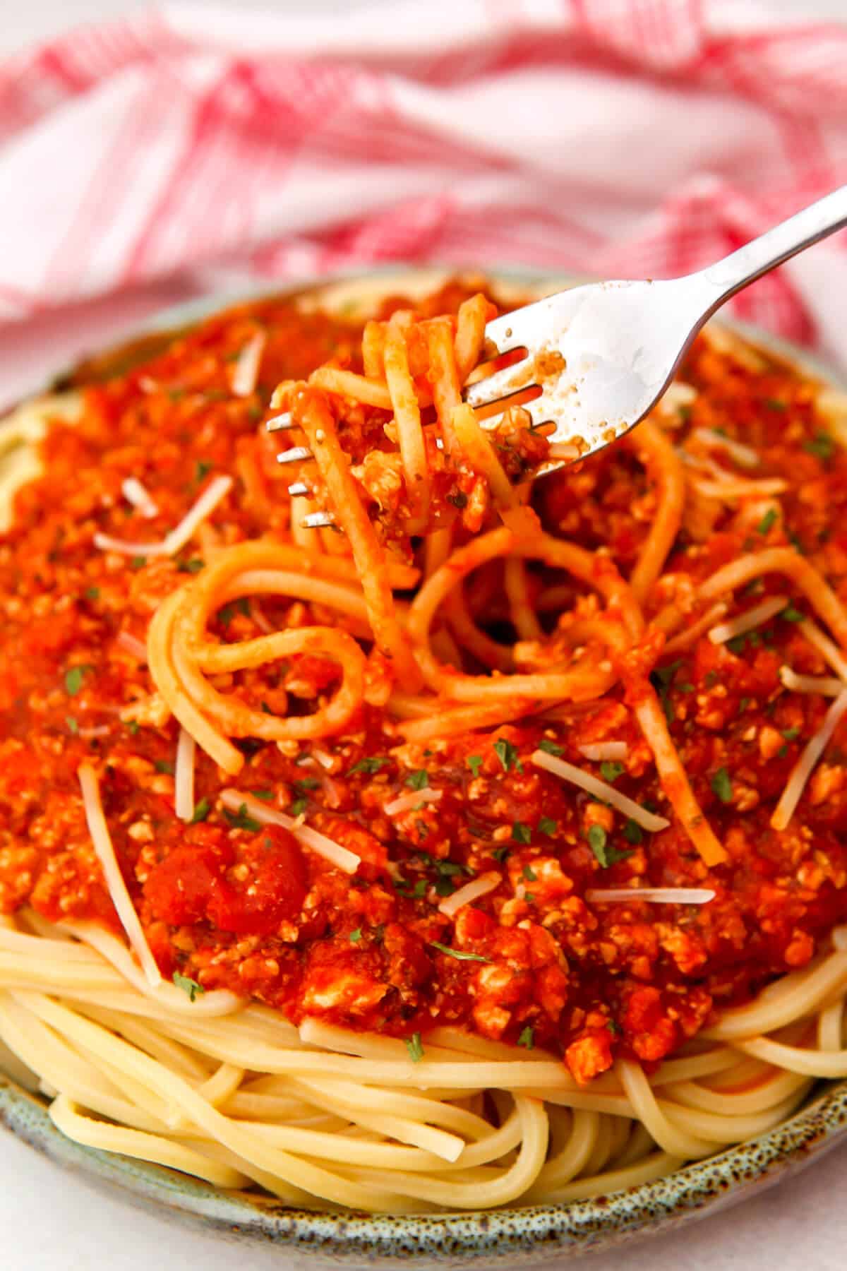 A plate full of spaghetti with tofu Bolognese served on top with someone scooping up a bite.