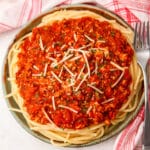 A plate of spaghetti topped with tofu Bolognese with a fork on the side.