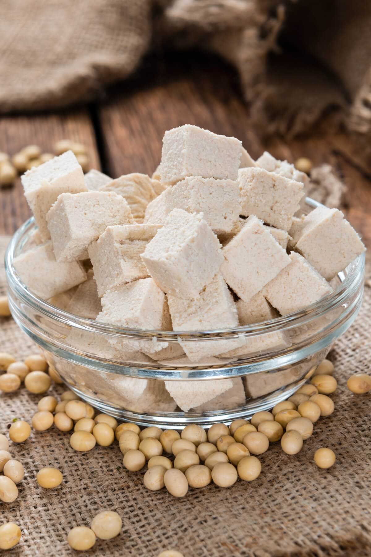 A glass bowl filled with cubes of uncooked tofu with soy beans around it.