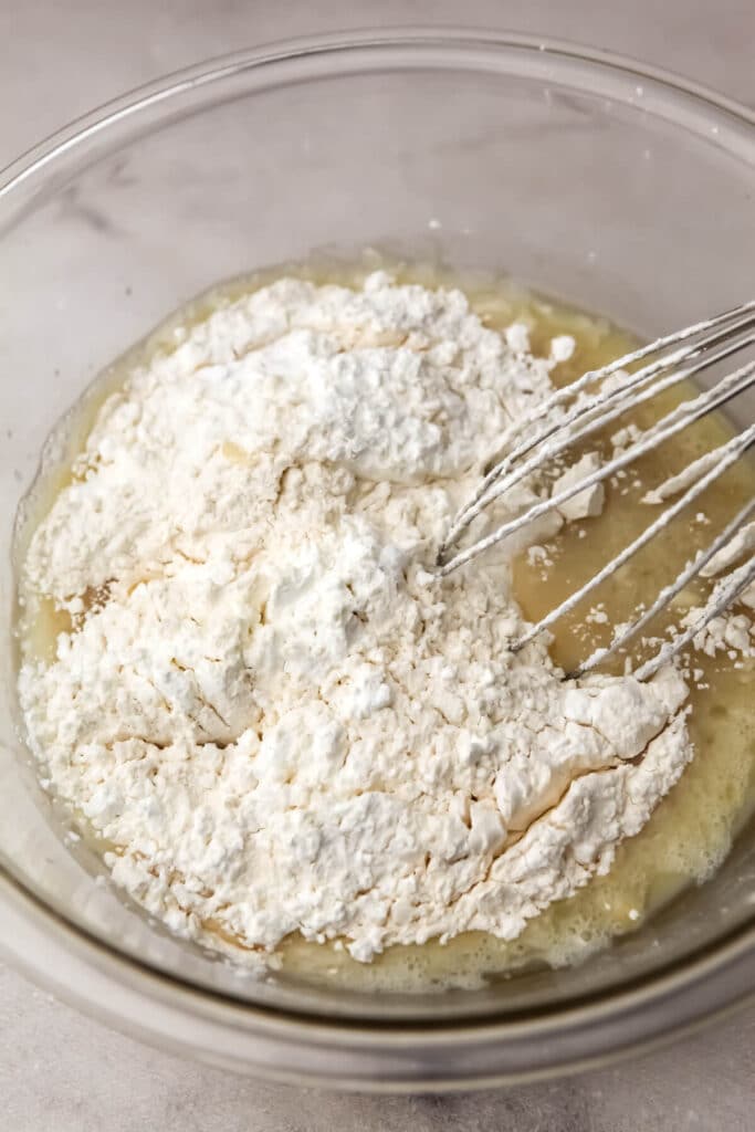 Wet and dry ingredients for vegan cupcakes in a mixing bowl with a whisk.