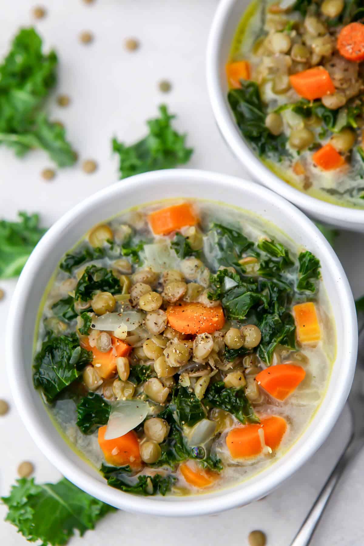 A close up of two bowls of lentil soup with carrots and kale.