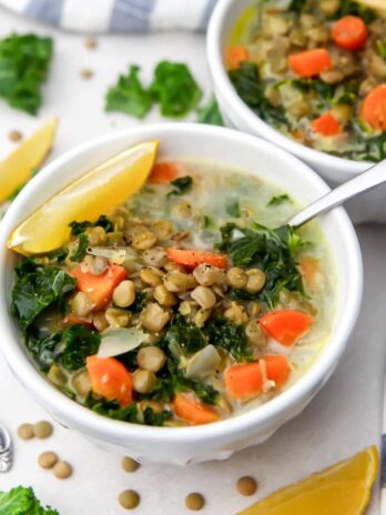 Creamy vegan lentil soup with carrots and kale with lemon wedges on the side.
