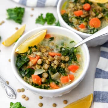 Creamy vegan lentil soup with carrots and kale with lemon wedges on the side.