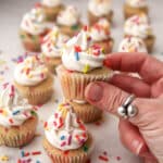 Vegan mini cupcakes with sprinkles on top with a hand holding up one small cupcake.