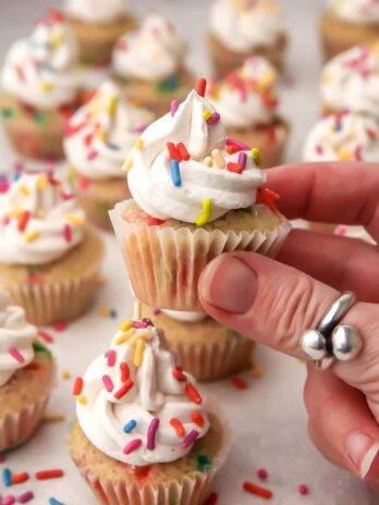 Vegan mini cupcakes with sprinkles on top with a hand holding up one small cupcake.