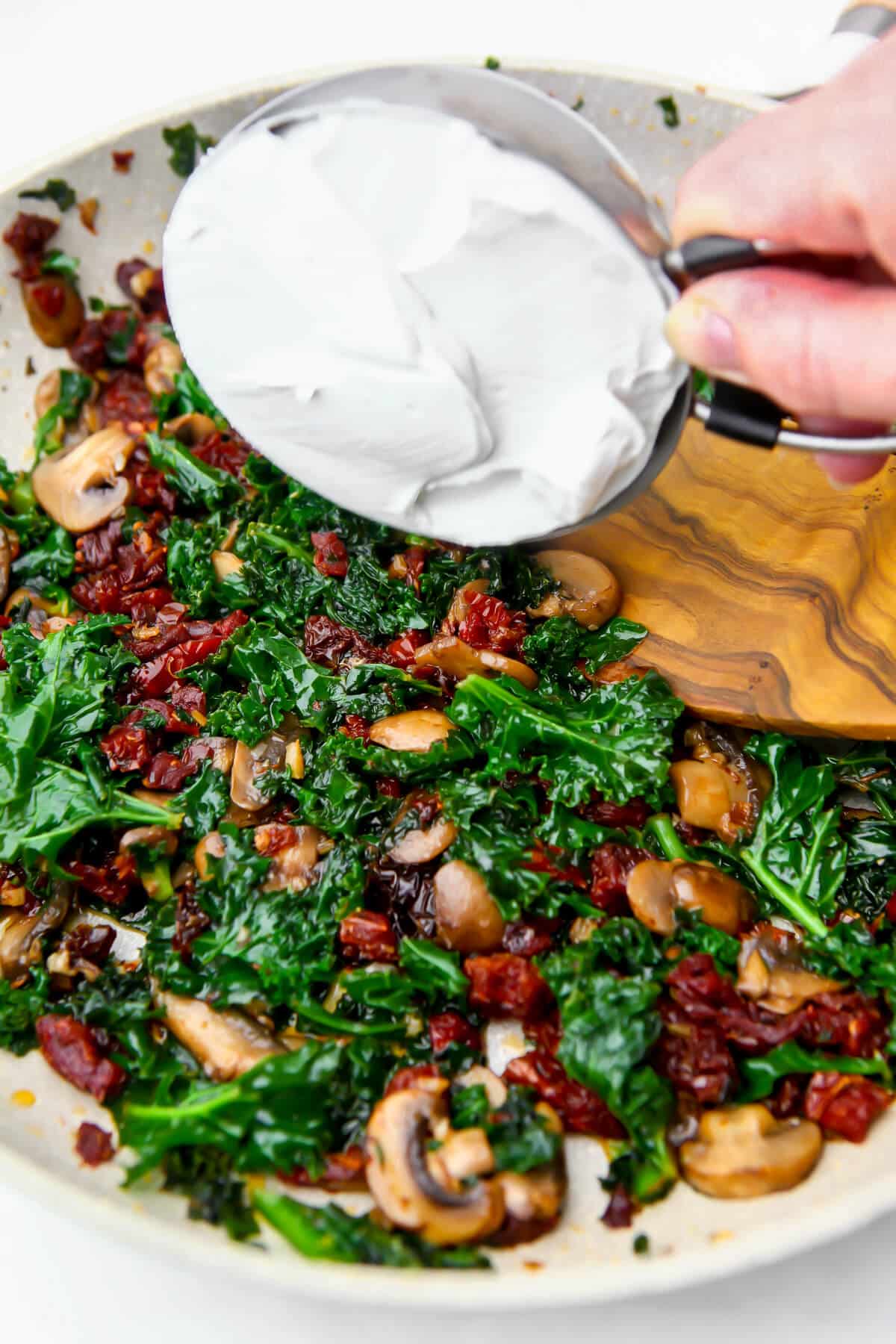 Sautéed mushrooms, kale, and sundried tomatoes with a scoop of cream being added.