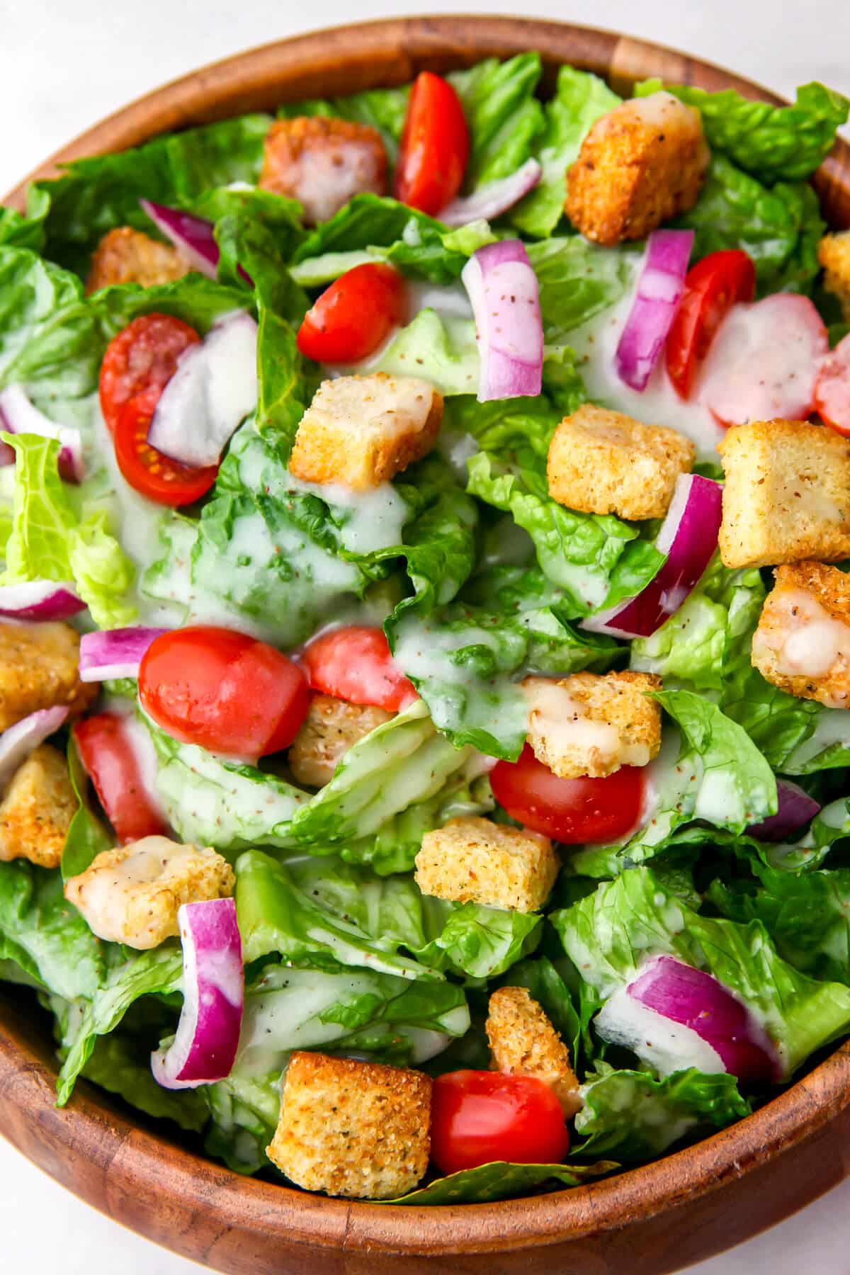 A salad with lettuce, cucumbers, tomatoes, croutons, and sweet onion dressing on top.