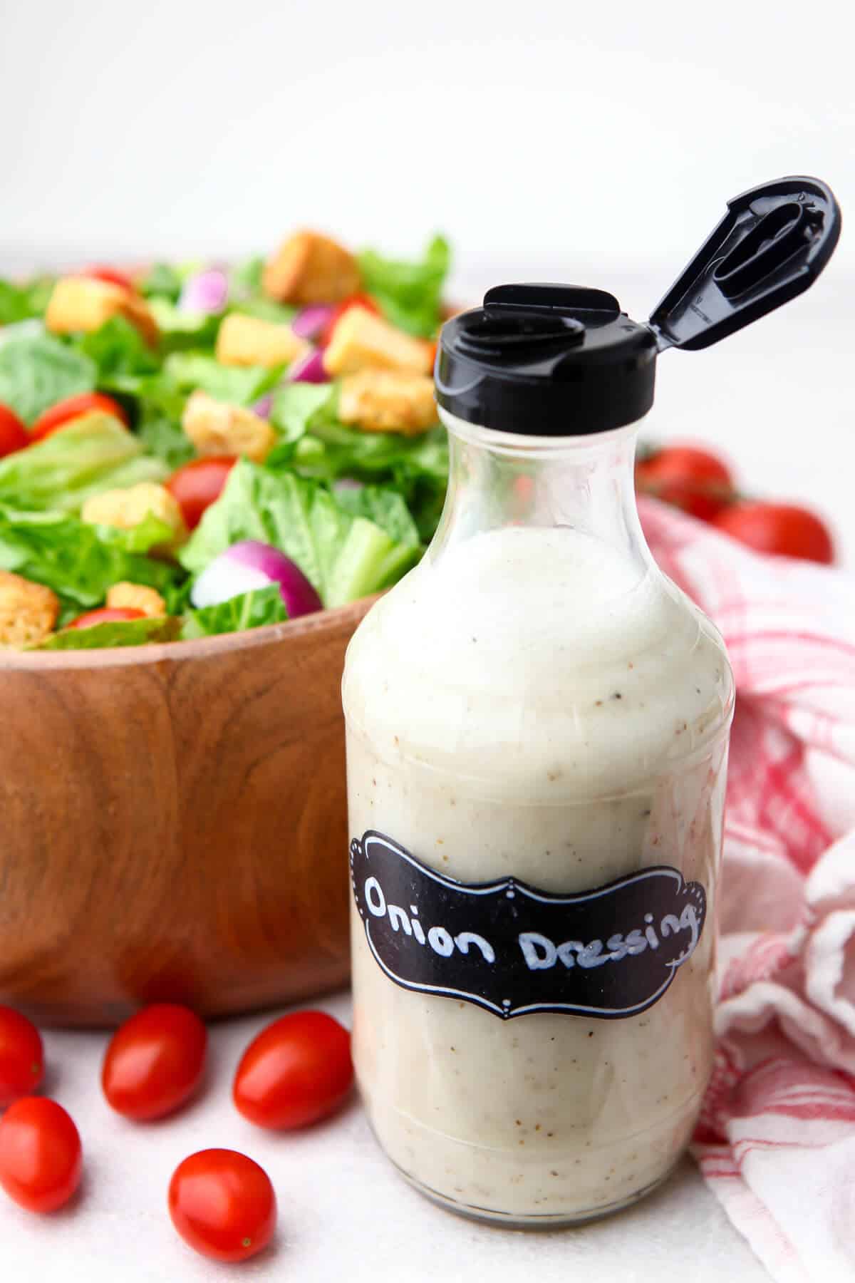Vegan sweet onion dressing in a bottle in front of a wooden bowl filled with salad.