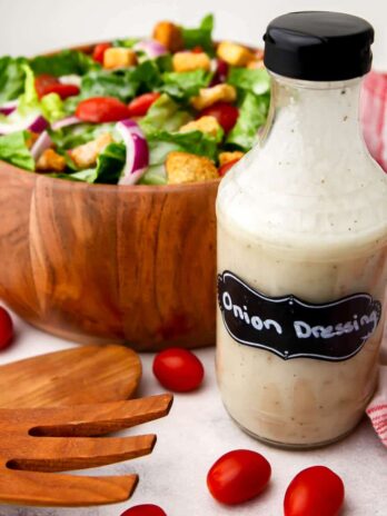 A bottle of sweet onion dressing in front of a salad with a tea towel on the side.