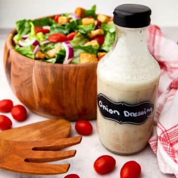 A bottle of sweet onion dressing in front of a salad with a tea towel on the side.