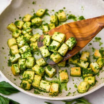 Pesto tofu in a frying pan being stirred with a wooden spatula.
