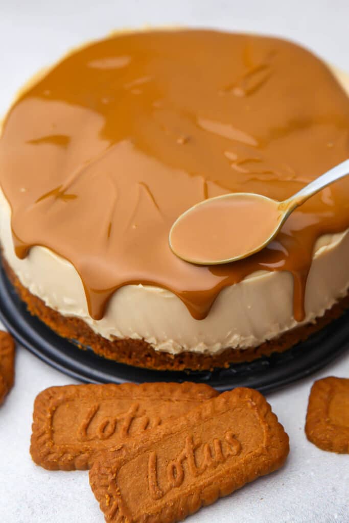 Using a spoon to make drips of cookie butter off the sides of the cheesecake.