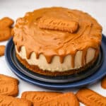 A vegan biscoff cheesecake with biscoff cookie butter on top and dripping over the edges with biscoff cookies around it.