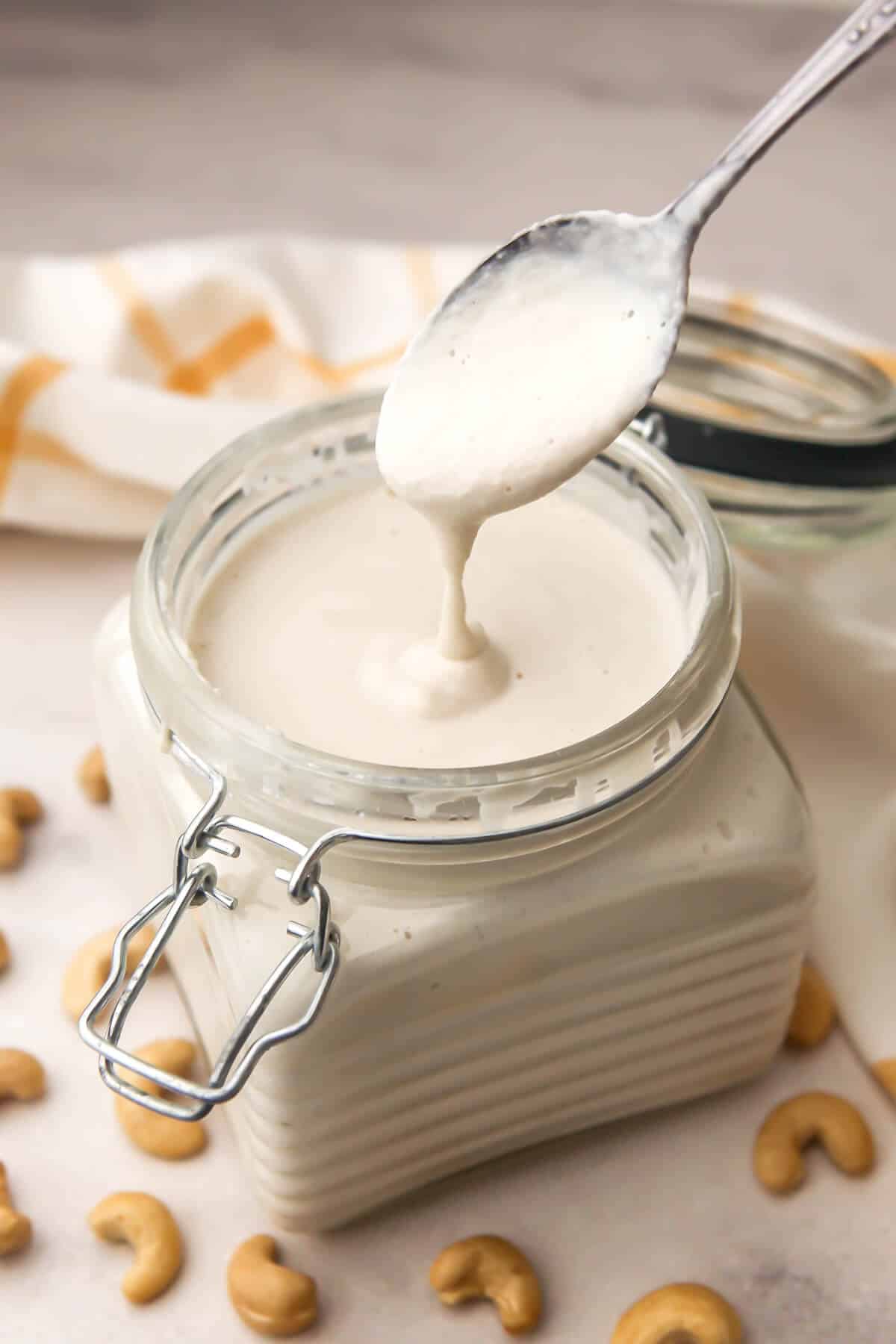 A glass jar filled with vegan heavy cream with cashews around it and a spoon over it.