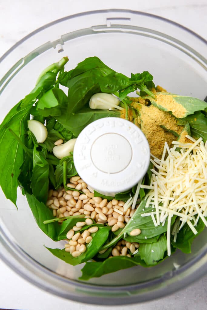 Fresh basil leaves, pine nuts, nutritional yeast, vegan parm, and salt in a food processor.