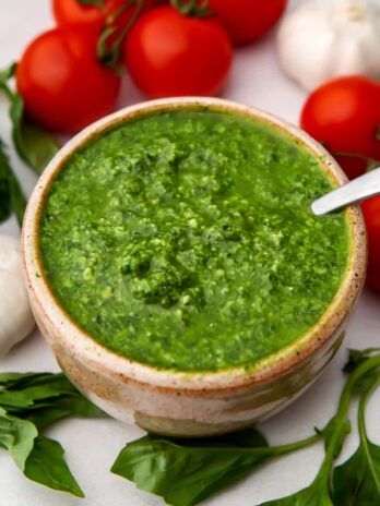 A top view of a bowl of vegan pesto with fresh basil, garlic, and tomatoes around it.