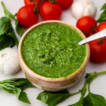 A top view of a bowl of vegan pesto with fresh basil, garlic, and tomatoes around it.