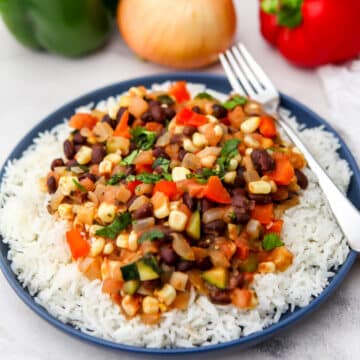 Mexican stir-fried veggies served over a bed of rice on a blue plate.