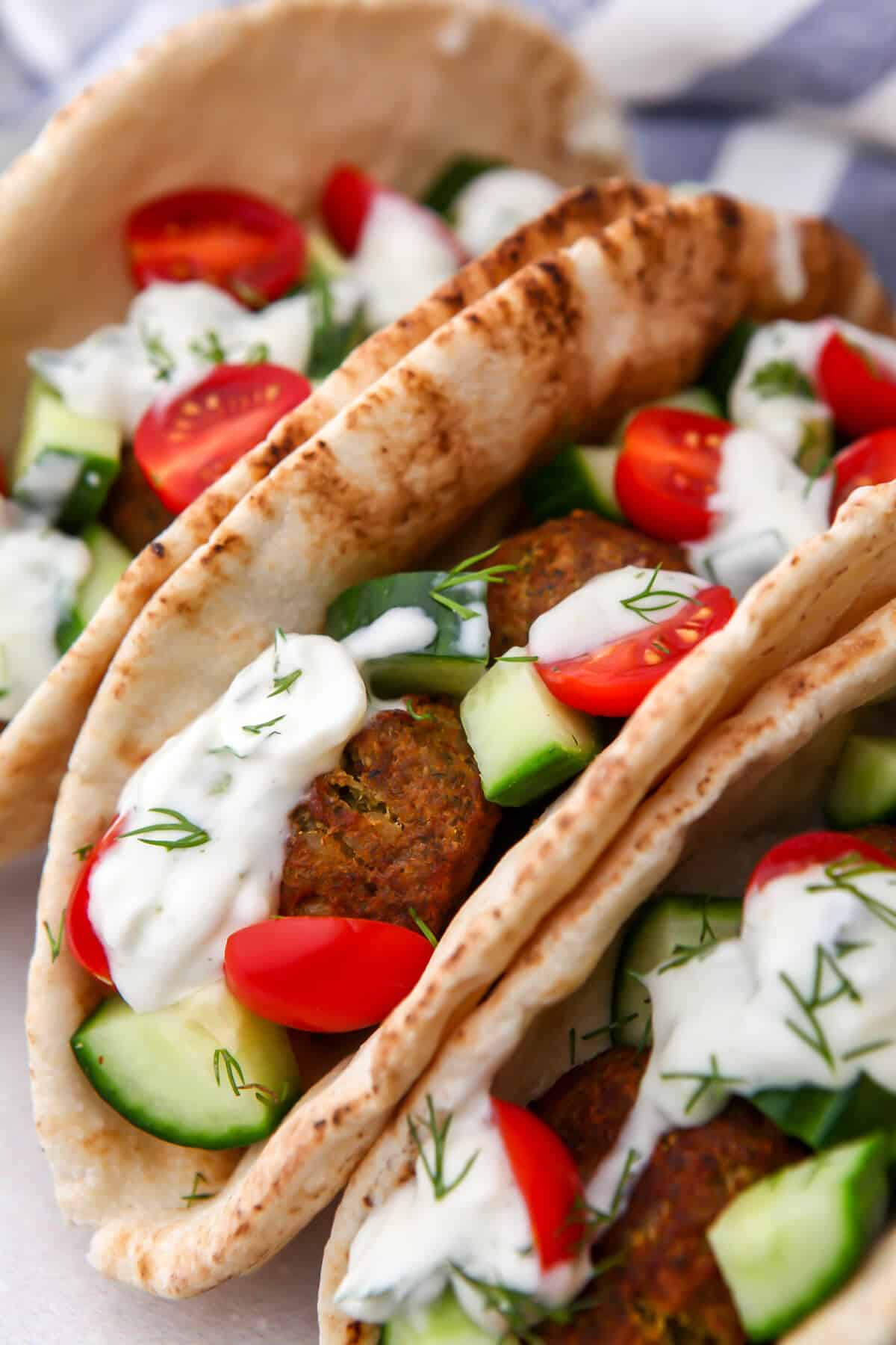 A close up of falafel gyro sandwiches made with pita bread and falafel with cucumbers and tomatoes on top.