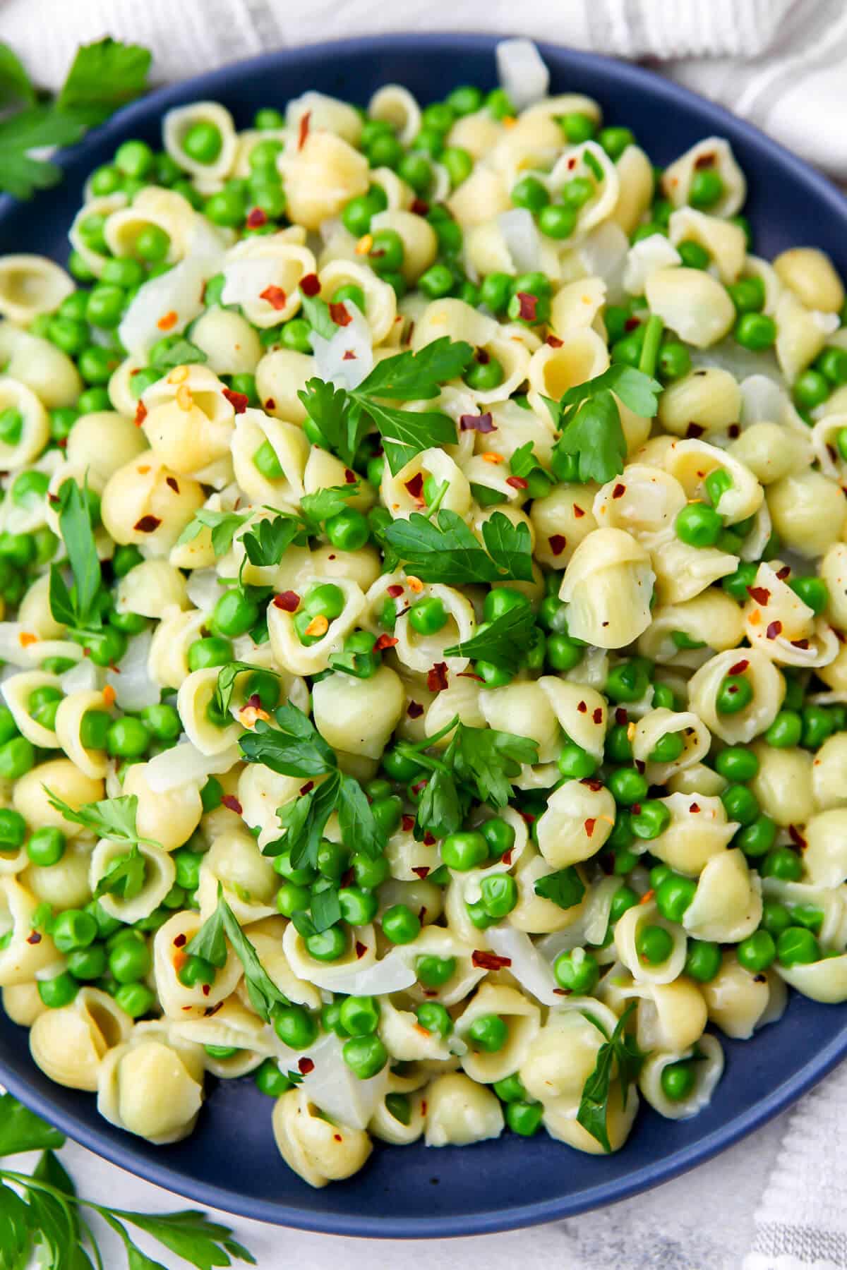 A top view of a plate full of pasta and peas garnished with parsley and red pepper flakes.