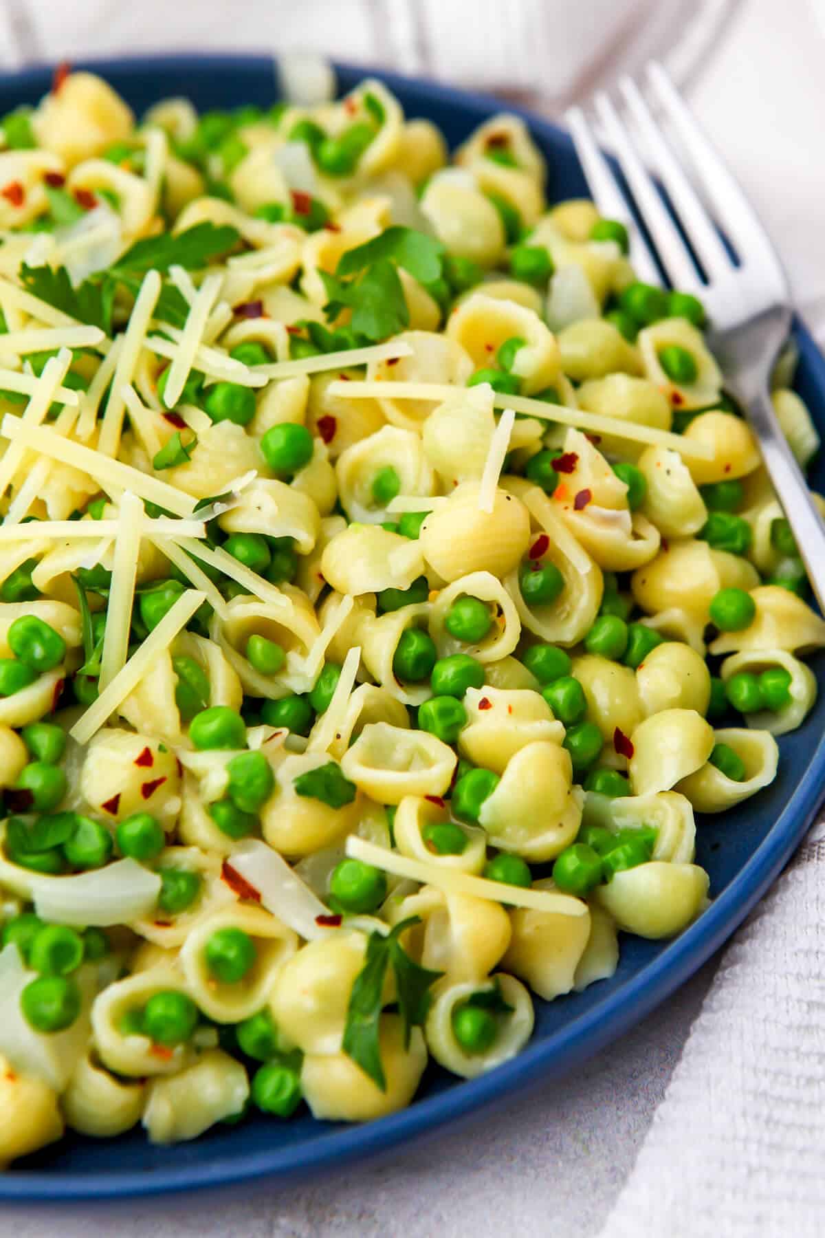 A blue plate filled with green pea pasta with a fork on the side.
