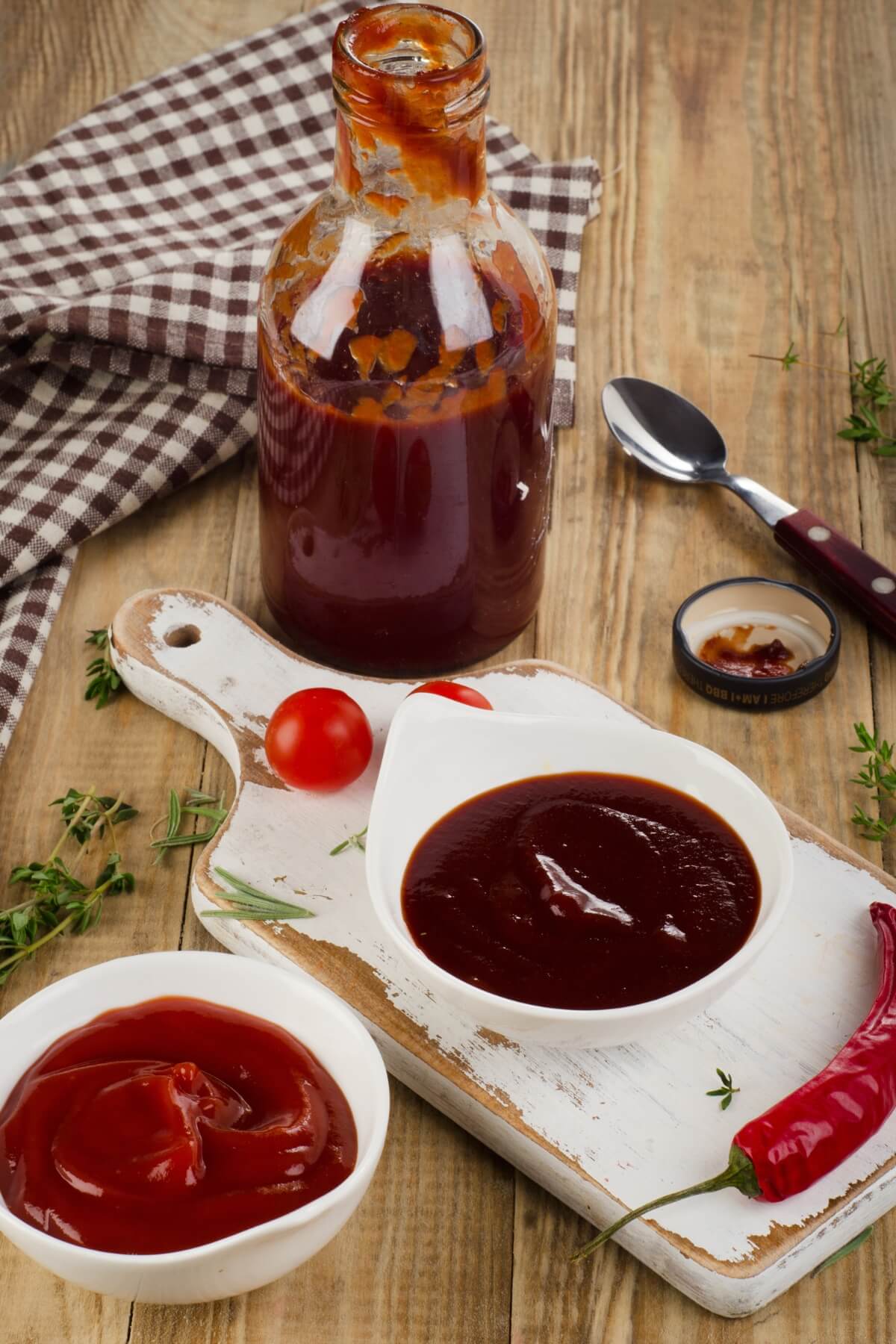 A bottle of BBQ sauce with bowls of BBQ sauce in front of it.
