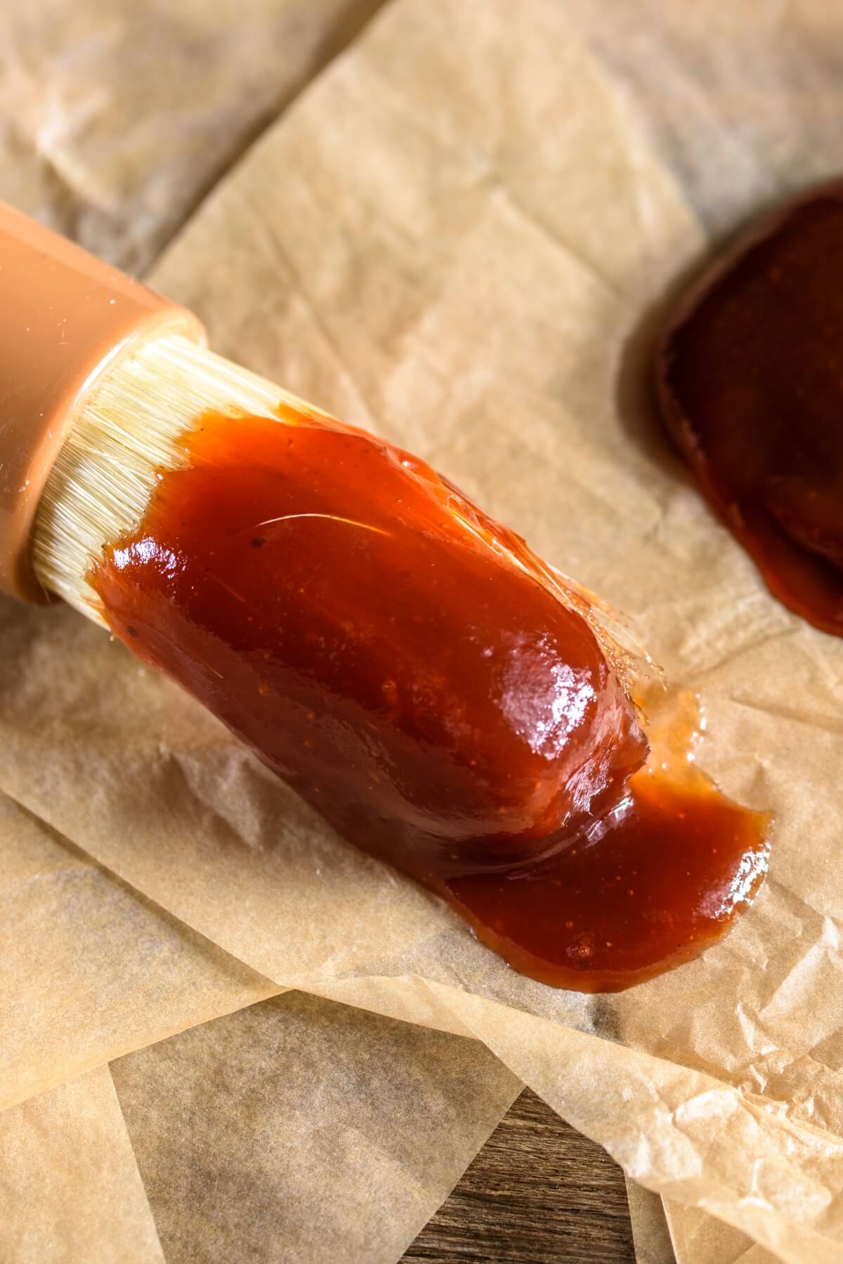 A brush with barbeque sauce on it on a piece of parchment paper.