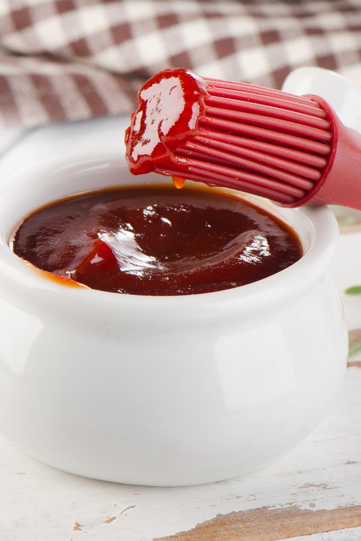A white bowl filled with vegan BBQ sauce and a red brush on the side.