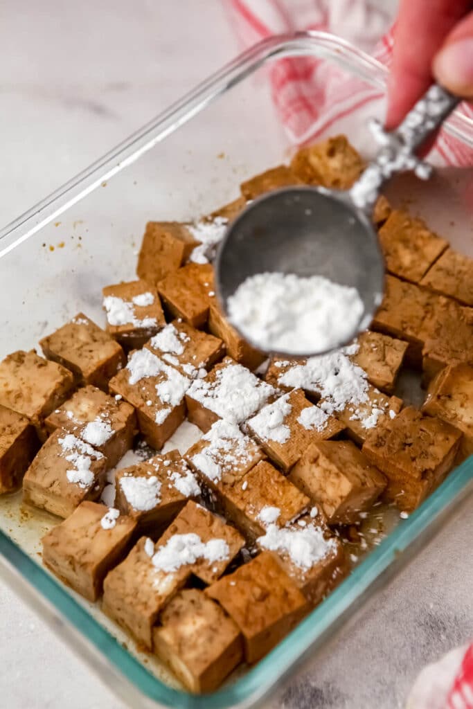 Cornstarch being sprinkled on the marinated tofu to make it crispy when fried.