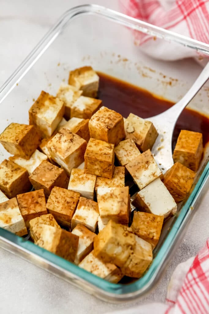 Tofu cubes soaking in an easy marinade being flipped with a spatula.