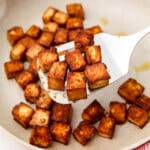 Marinated tofu in a white skillet with a spatula