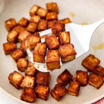 Marinated tofu in a white skillet with a spatula
